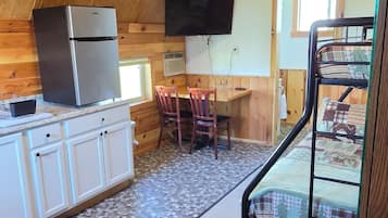 A rustic cabin with a kitchenette, a dining area, and a bunk bed.