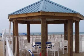 Relax in this serene beachside gazebo, surrounded by a wooden deck and offering a tranquil space for dining or unwinding.