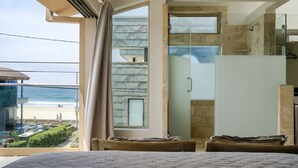 Habitación moderna con un amplio ventanal con vistas a una playa, ducha de vidrio y cama con vistas.