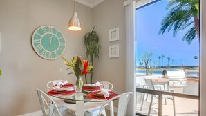 A dining area with a glass table, white chairs, a clock, and a view of the outdoors. - Paradise Retreat | 2BR Bayfront w/ Spacious Patio (San Diego)
