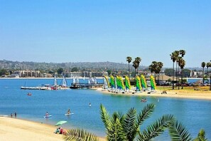 A beach with palm trees, a marina, and sailboats.