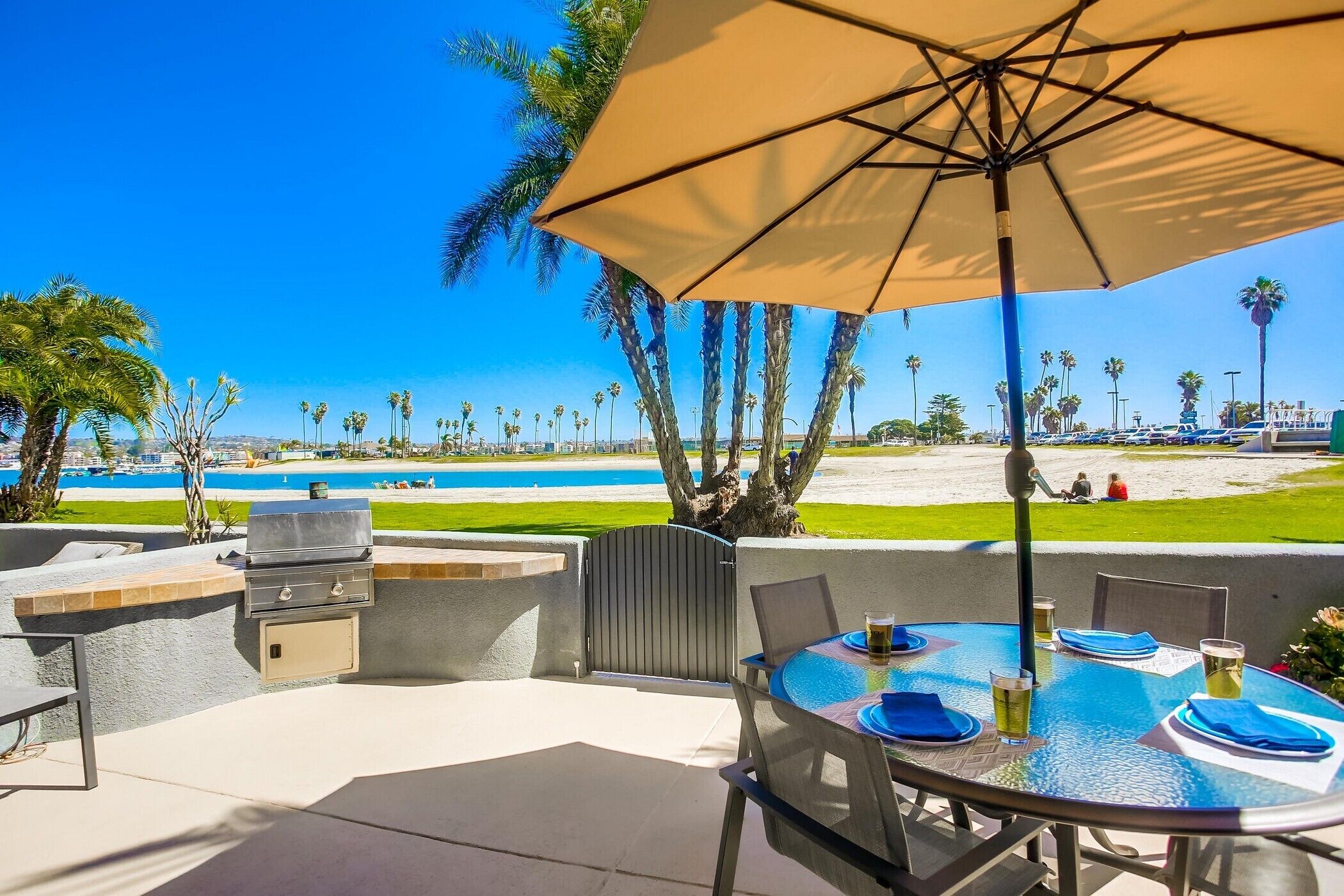 An outdoor patio with a grill, table, and umbrella overlooking a beach.