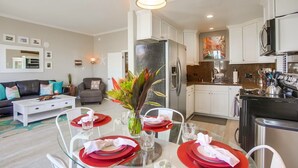 A modern kitchen with white cabinets, stainless steel appliances, and a dining area set for four with red placemats and clear glassware. - Paradise Retreat | 2BR Bayfront w/ Spacious Patio (San Diego)