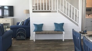 Un salon avec un canapé bleu, un banc avec des coussins bleus, un téléviseur et un escalier menant à un niveau supérieur.
