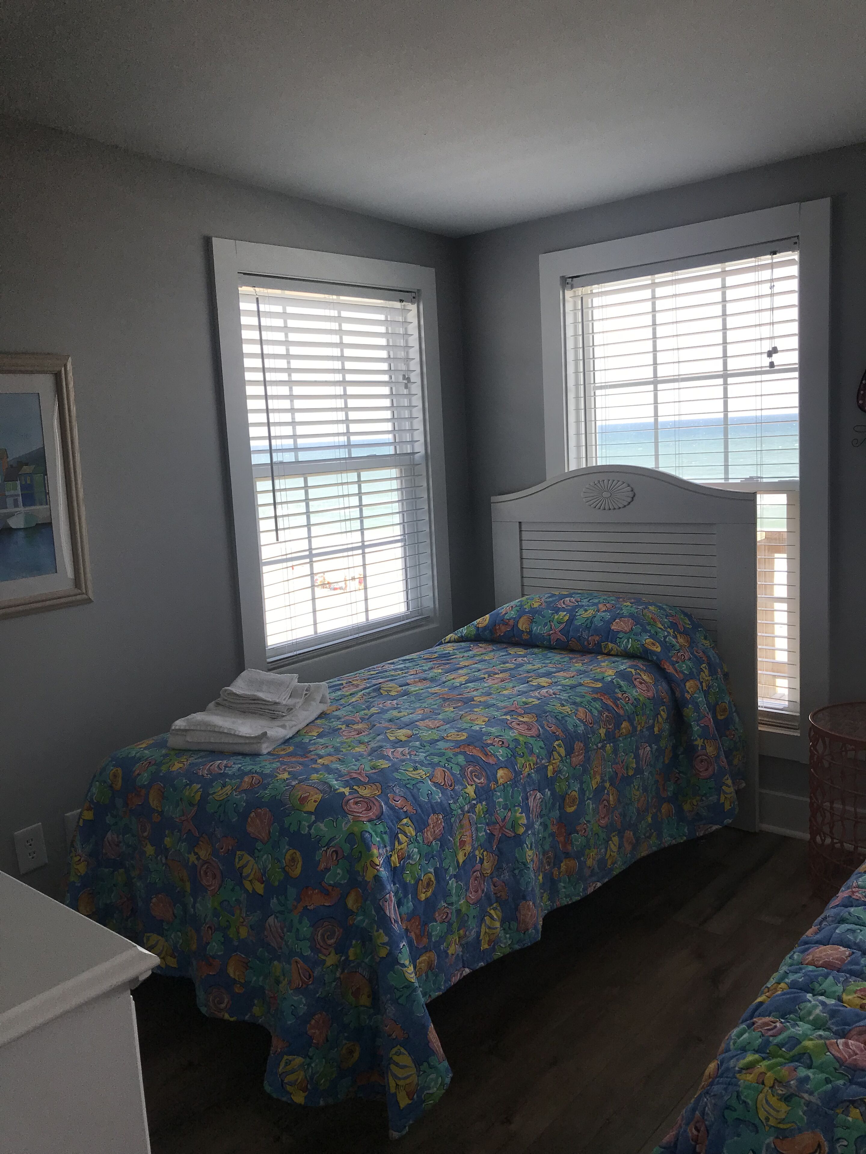 A bedroom with a bed, a window with blinds, and a view of the sea.