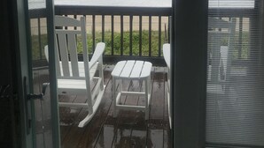 Vue depuis une terrasse couverte avec une porte vitrée, donnant sur l’océan. On y trouve deux chaises Adirondack blanches et une petite table.