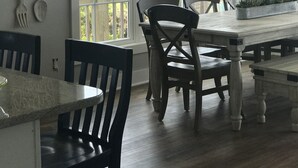 Un coin repas avec une grande fenêtre, des chaises en bois, une table et un luminaire suspendu.