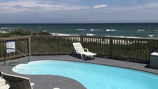 Une terrasse en bois avec une piscine, des chaises longues et une vue sur l’océan.