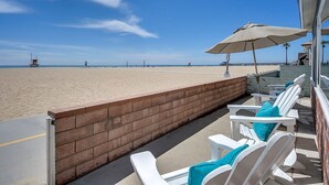 A beachside patio with white lounge chairs and a beige umbrella, overlooking a sandy beach and ocean. - BEACHFRONT GETAWAY ON THE SAND (Newport Beach)