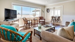 A spacious living room with a television, wicker chairs, a coffee table, and a view of the beach through large windows. - BEACHFRONT GETAWAY ON THE SAND (Newport Beach)