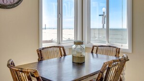 A dining area with a table and chairs, a clock on the wall, and a view of the beach through large windows. - BEACHFRONT GETAWAY ON THE SAND (Newport Beach)
