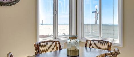 Un comedor con una mesa y sillas, un reloj en la pared y vistas a la playa a través de amplios ventanales.
