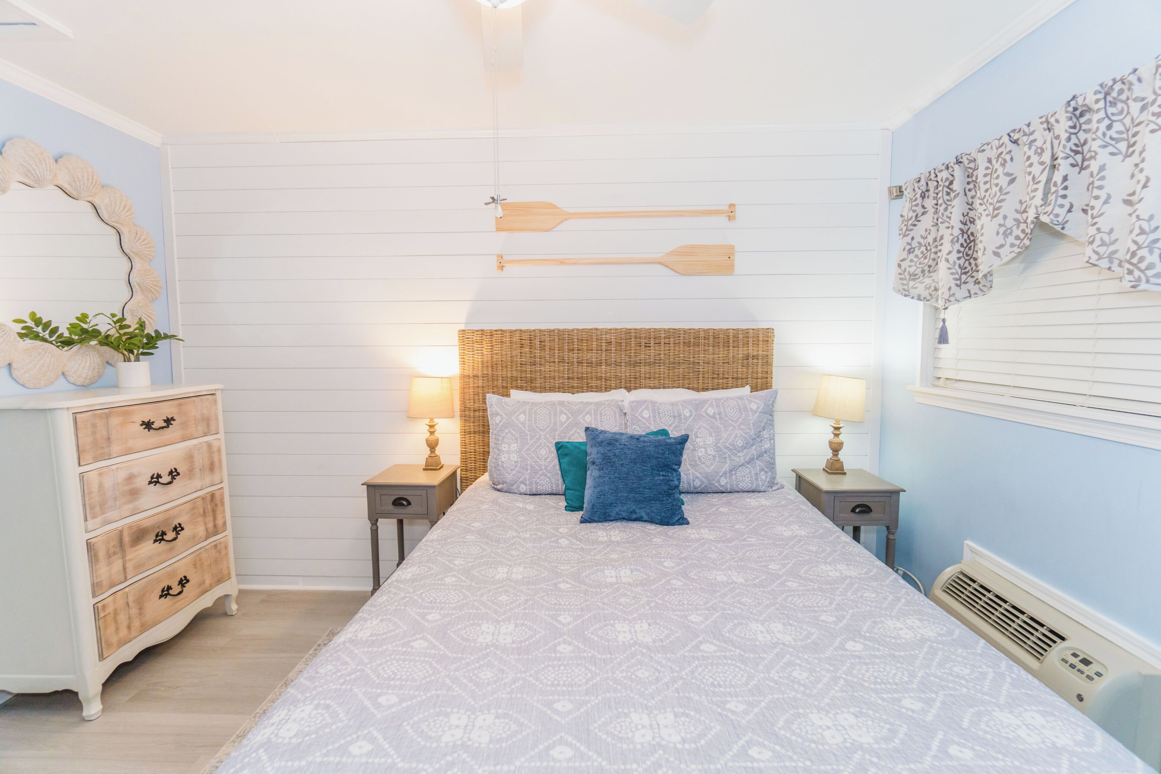 A bedroom with a bed, two nightstands, a dresser, a mirror, and a wall-mounted shelf.