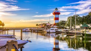 A marina with boats docked, a lighthouse, and a building with a green roof.