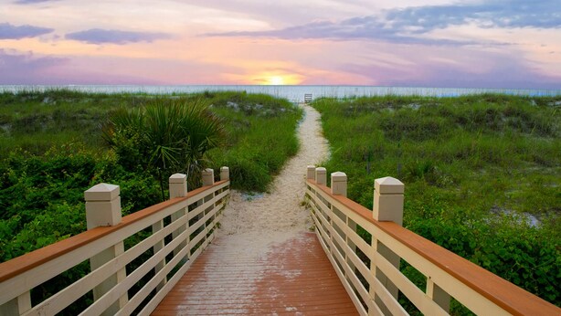 A wooden boardwalk leading to a beach with a sunset in the background.