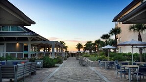 A pathway leading to outdoor seating areas with tables and chairs, surrounded by palm trees and plants.