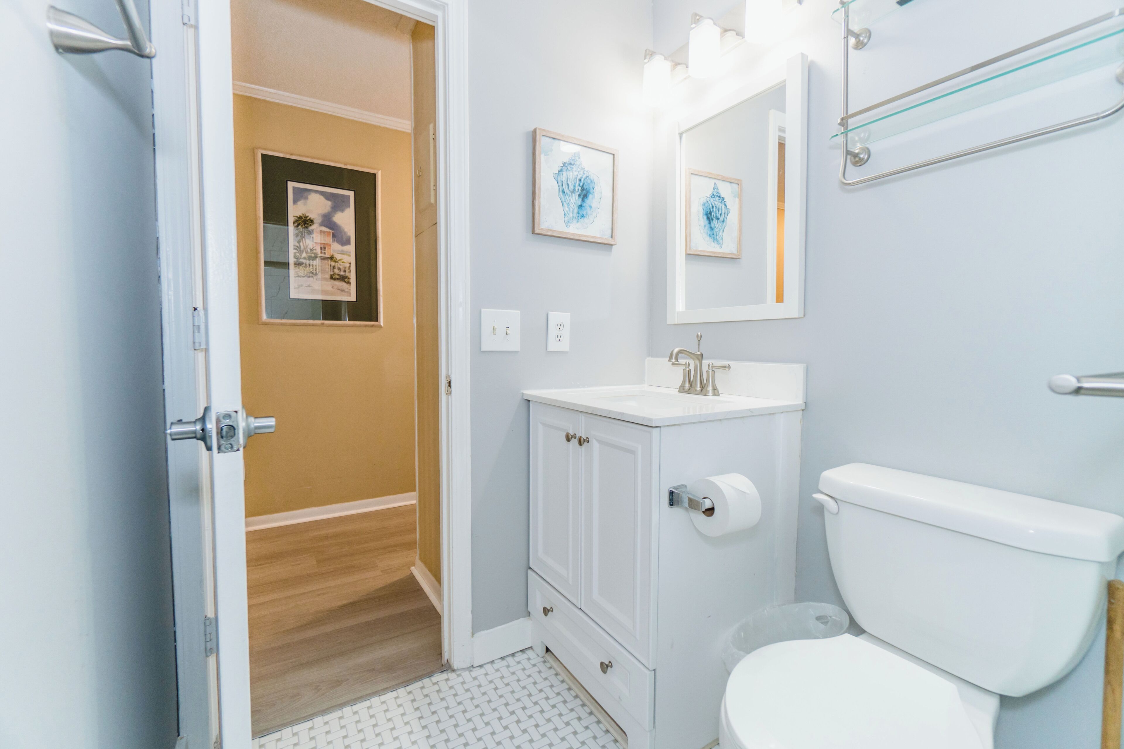 A bathroom with a toilet, sink, and mirror. There is a door leading to another room.
