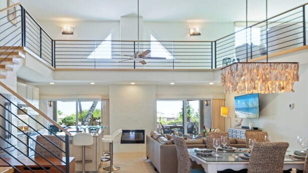 Ein großzügiges, modernes Interieur mit hoher Decke, einem Essbereich mit Korbstühlen, einer Küche mit Bar und einer Treppe, die zu einer oberen Ebene führt.