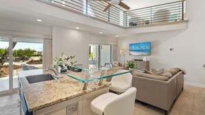 Eine moderne Küche mit einer Glasinsel, ein Essbereich mit einer Couch und ein Balkon mit Geländer.