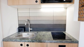 Una cocina con un lavamanos de acero inoxidable, un microondas encima y una placa vitrocerámica integrada.