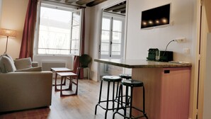 Un espacio habitable compacto con cocina, sofá, mesa de comedor y televisor en la pared.