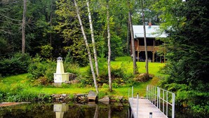 Una cabaña con un muelle que se adentra en un estanque, rodeada de un bosque denso.