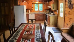 Una cocina rústica de cabaña con una mesa de comedor, sillas y un refrigerador.