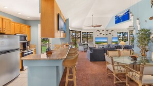 A modern kitchen with a central island, wooden cabinets, and a large window overlooking a scenic view. - Sale!! Gorgeous 3BR 2BA Villa in Wailea, With Ocean, Golf and Sunset Views (Kihei)