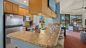 A modern kitchen with granite countertops, stainless steel appliances, wooden cabinets, and a large island with stools. - Sale!! Gorgeous 3BR 2BA Villa in Wailea, With Ocean, Golf and Sunset Views (Kihei)