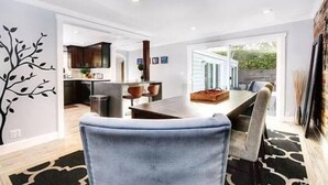 A modern dining area with a large table and chairs, a kitchen in the background, and a view of the outdoors. - Villa Laguna -- ocean views, walkable, and new (Laguna Beach)