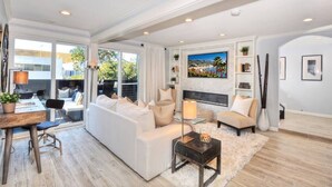 A spacious living room with a white sofa, a fireplace, and a large TV. - Villa Laguna -- ocean views, walkable, and new (Laguna Beach)