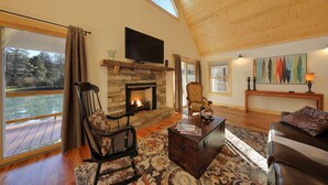 Una sala de estar acogedora con chimenea de piedra, techo de madera y grandes ventanales con vistas a una terraza.