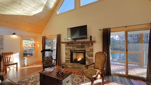 Amplia sala de estar con chimenea de piedra, techo de madera y ventanas grandes.