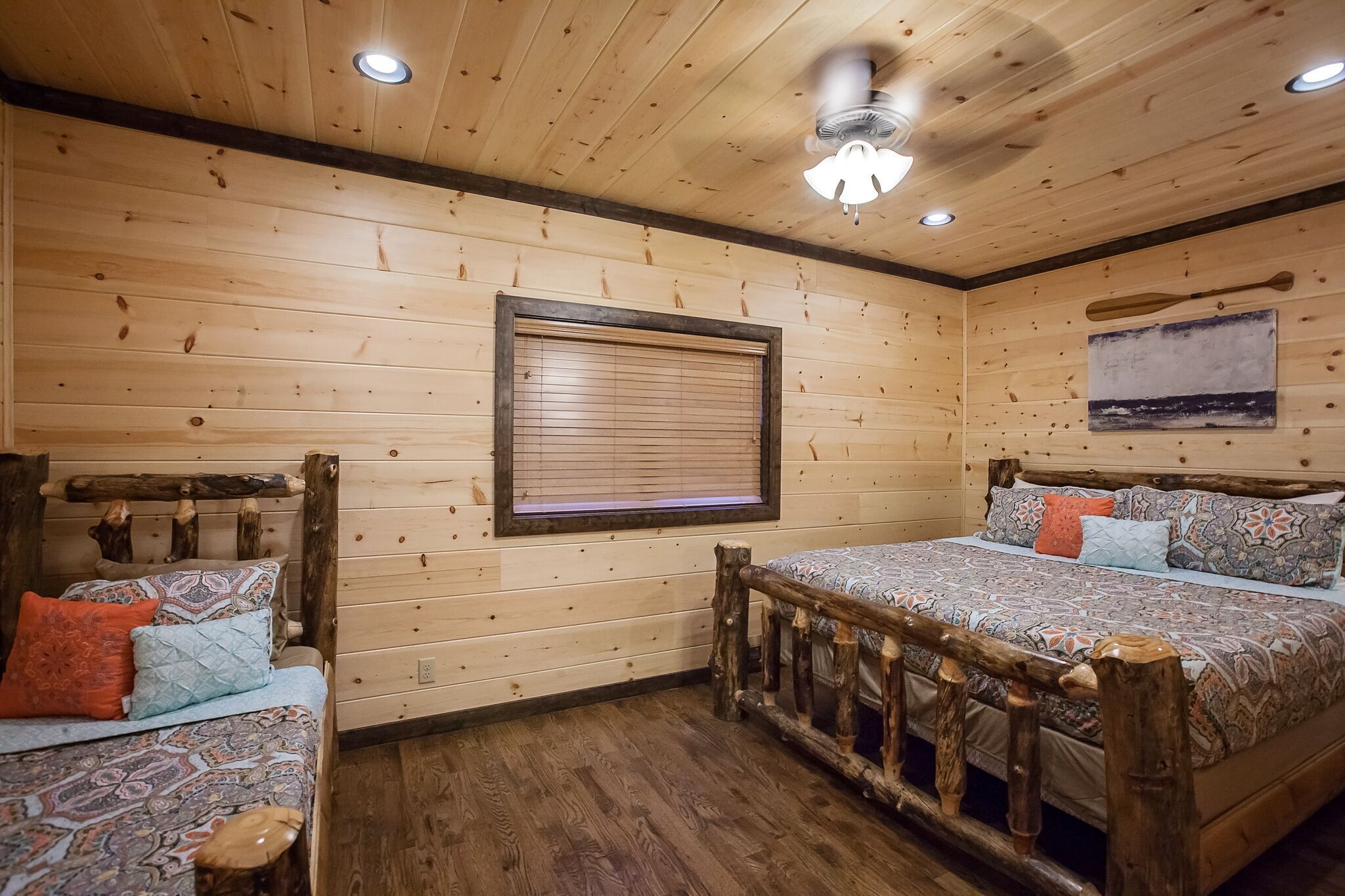 Une chambre dans un chalet en bois, avec deux lits, un ventilateur de plafond et une fenêtre avec des stores.