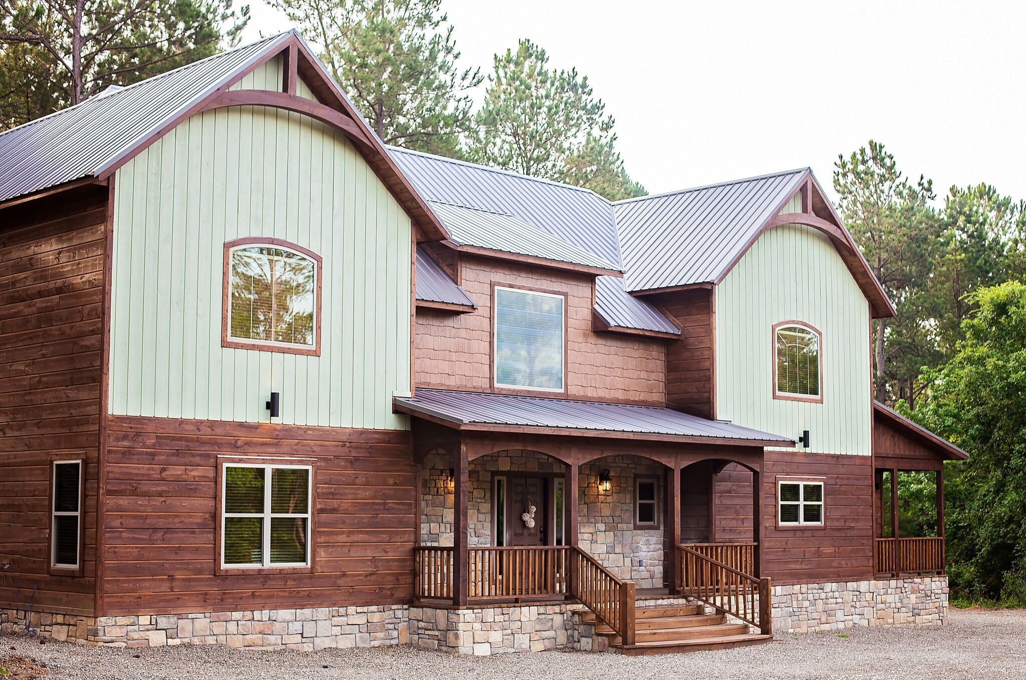 A large, two-story house with a stone foundation, wooden siding, and a metal roof.