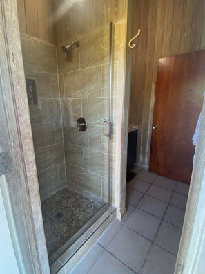 Shower features a glass door and a pebble-patterned floor with a drain.