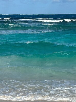 A beach with clear turquoise water and waves.