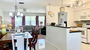 Uma cozinha moderna com armários brancos, uma ilha central e uma área de jantar com mesa e cadeiras.