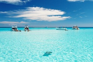 A clear turquoise sea with several boats and a stingray visible.
