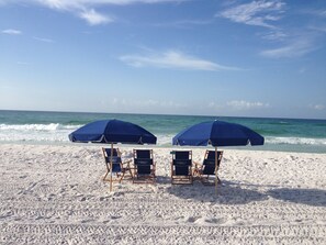 A beach with two blue umbrellas and four beach chairs.