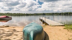 Vista para um lago com um píer, um barco coberto e uma praia de areia.