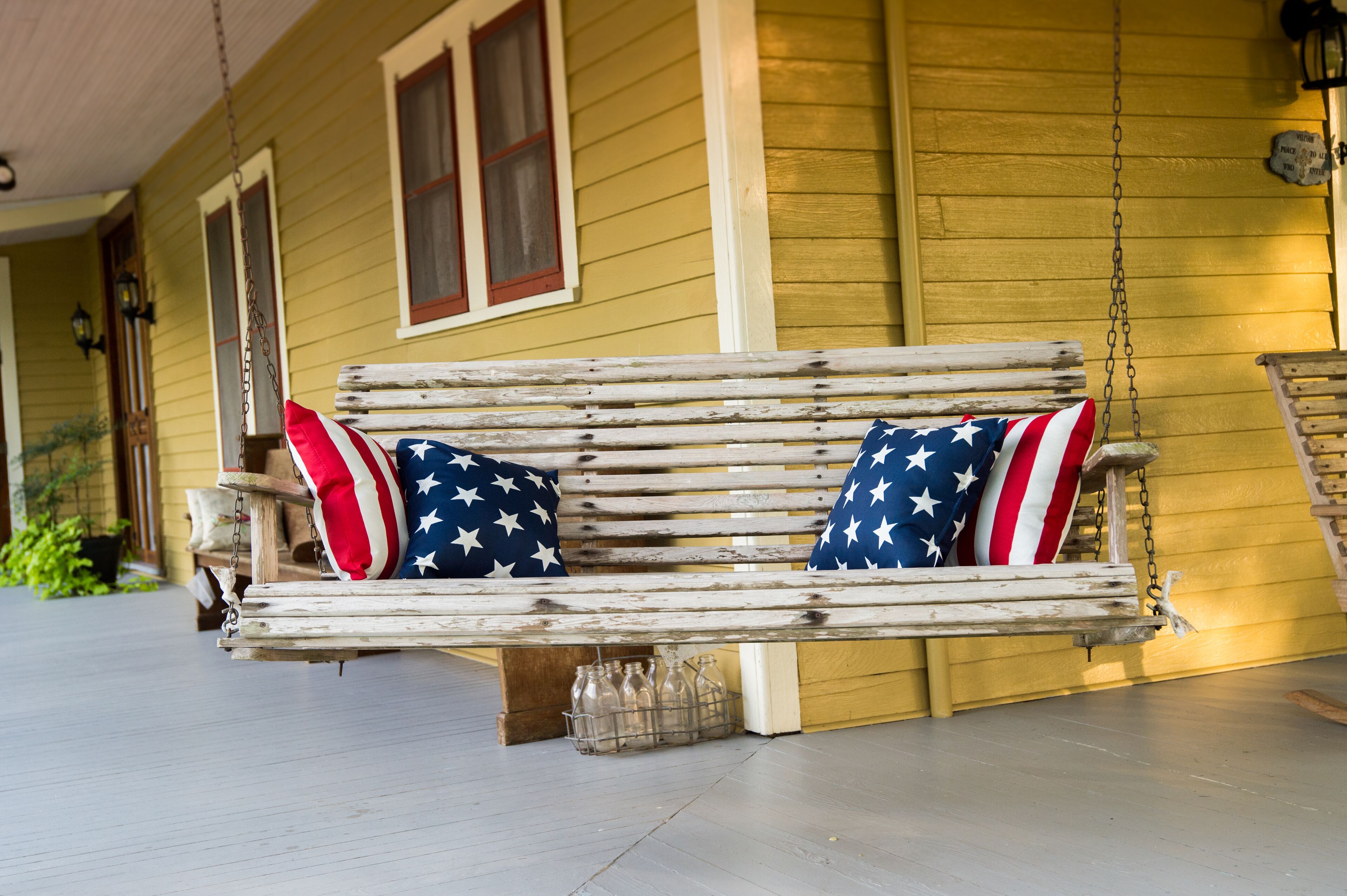 A porch with a wooden swing bench featuring American flag pillows.