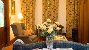 Una sala de estar acogedora con papel tapiz floral, un sofá cómodo, una mesa con un florero y una lámpara.