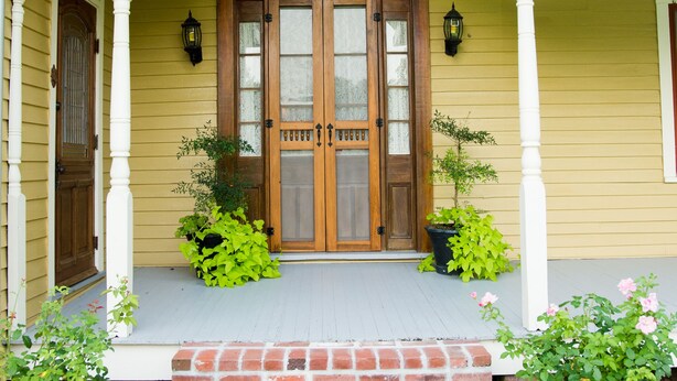 Una casa amarilla con puerta principal de madera, dos macetas y una escalera de ladrillo que conduce a la entrada.