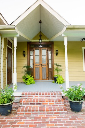A yellow house with a wooden front door, two potted plants, and a brick staircase leading to the entrance. - CAJUN HOSPITALITY -  LA PETITE VOIE DE ST. THERESE (St. Martinville)