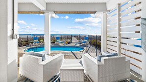 Un espace extérieur abrité avec une piscine, des meubles en osier blancs et une vue sur le ciel.