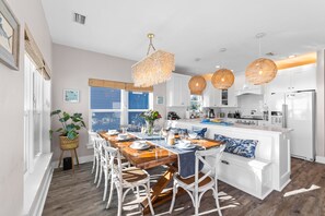 Une cuisine moderne avec des meubles blancs, une table à manger en bois et des suspensions en osier.