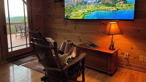 A wooden interior with a TV displaying a scenic landscape, a wooden desk with a lamp, and a chair. - Buck Mountain Getaway - Stunning views, hot tub, fireplace. Nearby Boone. (Purlear)