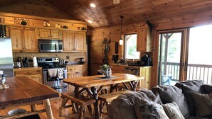 A cozy cabin-style kitchen with wooden cabinets, a dining table, and a couch. - Buck Mountain Getaway - Stunning views, hot tub, fireplace. Nearby Boone. (Purlear)