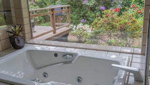 A bathroom with a bathtub, a potted plant, and a view of a garden with flowers and a wooden deck. - Family Friendly Home on 20 Acre Farm (Caspar)